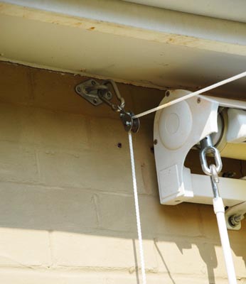 Stap 6 - Knoop een uiteinde van het touw strak om een van de karabijnhaken en bevestig de haak aan een D-ring op de hoek van uw schaduwdoek sla het andere uiteinde om de kikker op de mast (daarbij flink wat ruimte in het touw latend, het schaduwdoek moet echt slap blijven hangen).